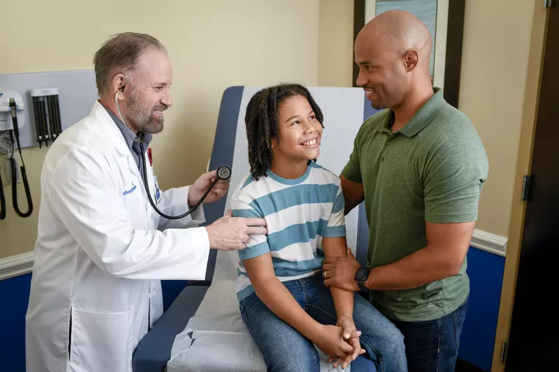 A Provider Checks a Child Patient's Breathing While His Father Supports Him