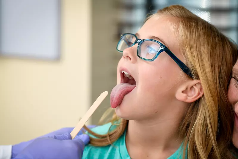 A Centra Care Patient Sticks Out Her Tongue as a Tongue Depressor Comes Into View 