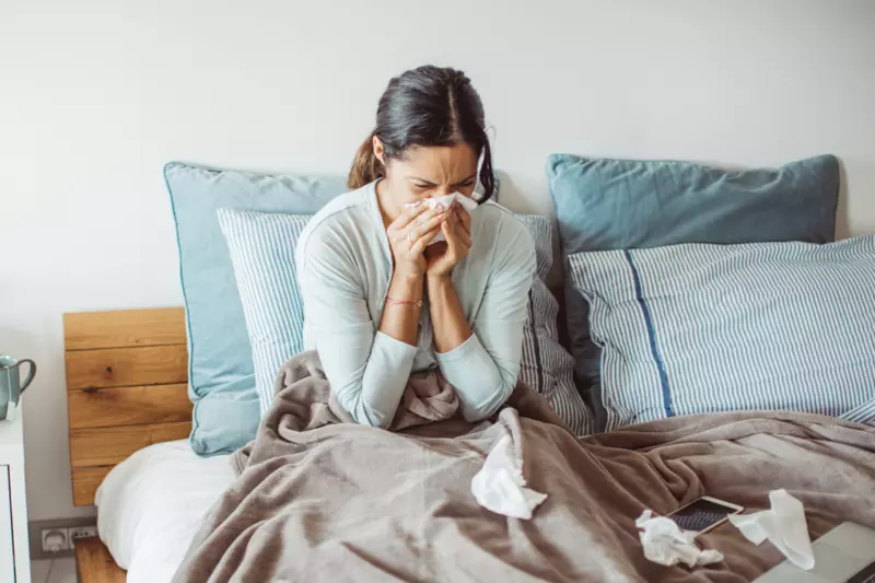 A Woman Blows Her Nose While Sitting Up in Bed