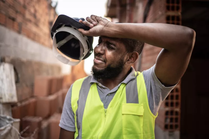 An Over Heated Construction Worker Removes His Hard Hat to Wipe His Brow