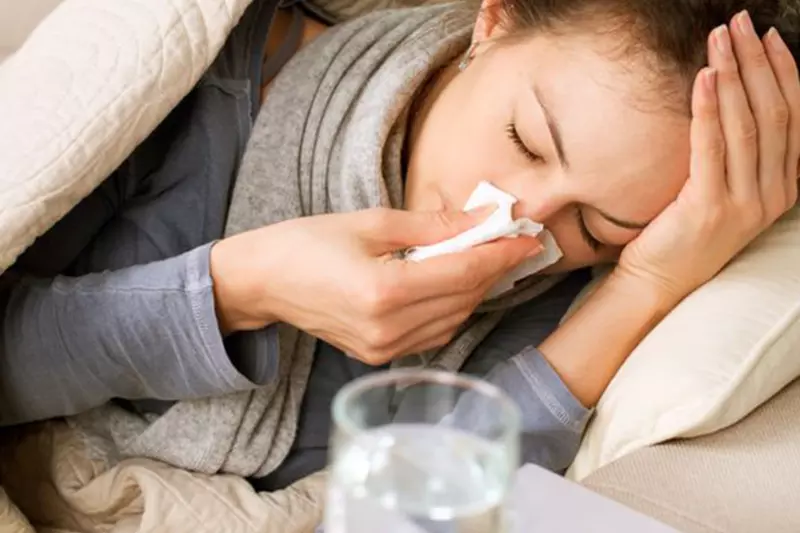 A woman laying in bed with the flu, water and medicine on her nightstand.