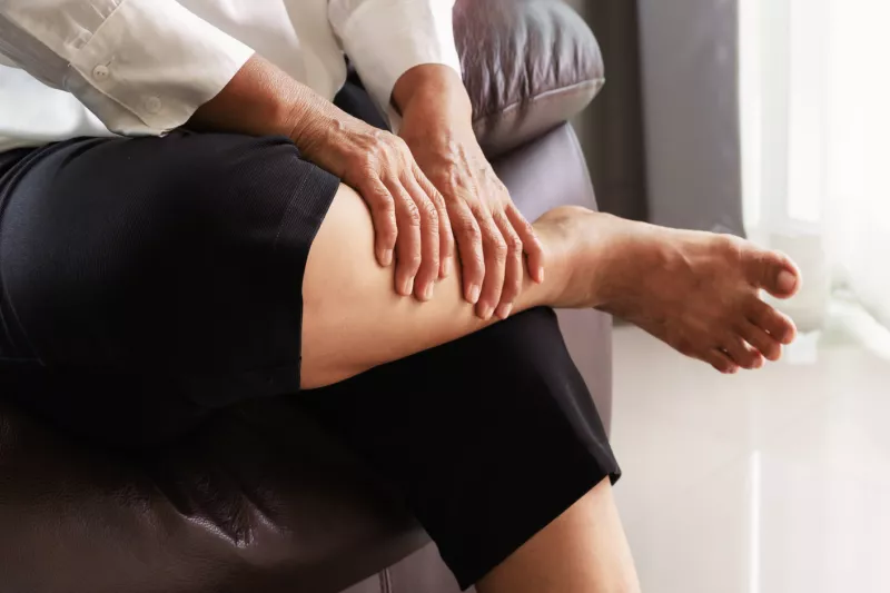 A person sitting down massaging their calf due to pain.