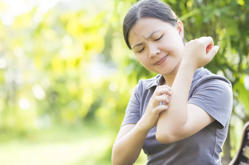 A woman scratches an itchy rash on her arm.