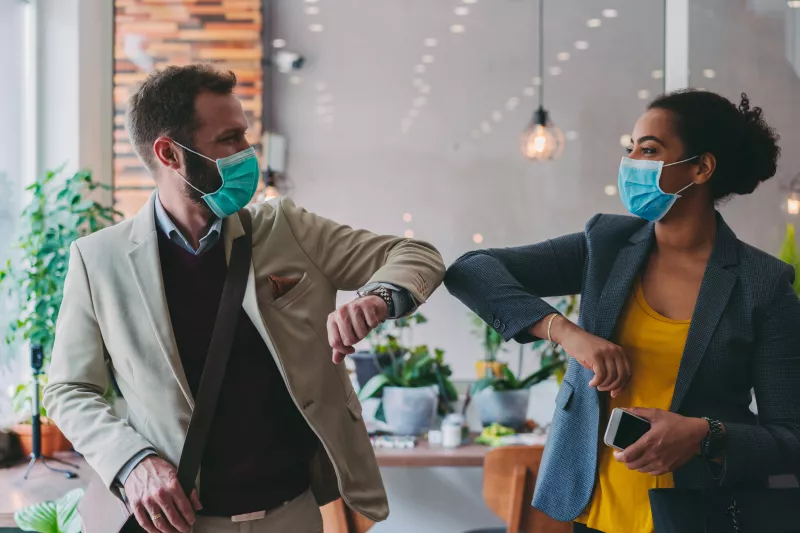 Masked coworkers elbow bump