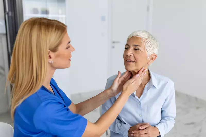 Doctor feeling the neck of a woman to check her thyroid.