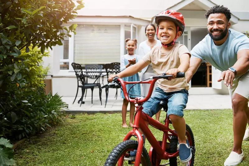 Family teaching son to ride bike in yard
