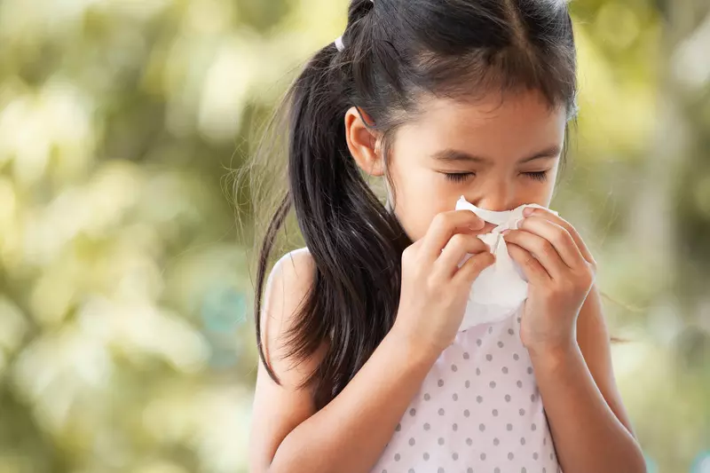 A little girl blows her nose into a tissue.