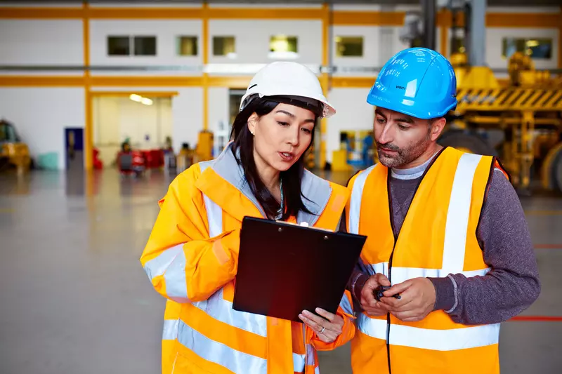 Two Warehouse Workers Talking Together Over a Clipboard.