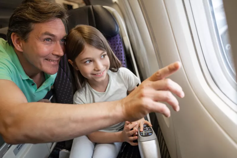 A father and daughter looking out the window of an airplane.
