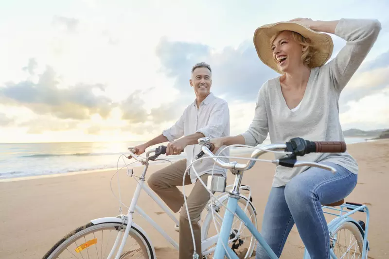 Man and woman in a hat riding bicycles on the beach at sunset. 