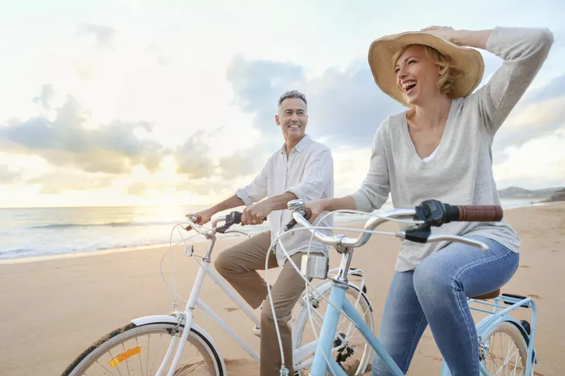 Man and woman in a hat riding bicycles on the beach at sunset.