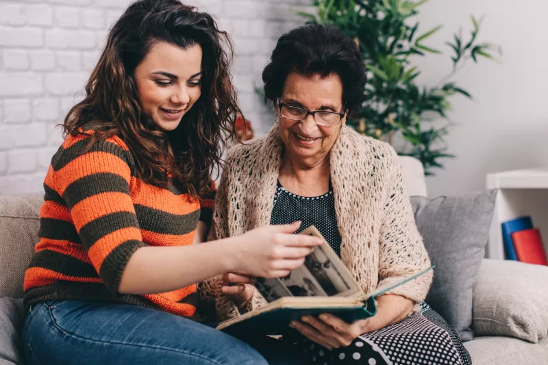 A grandmother and granddaughter look at a photo album together.