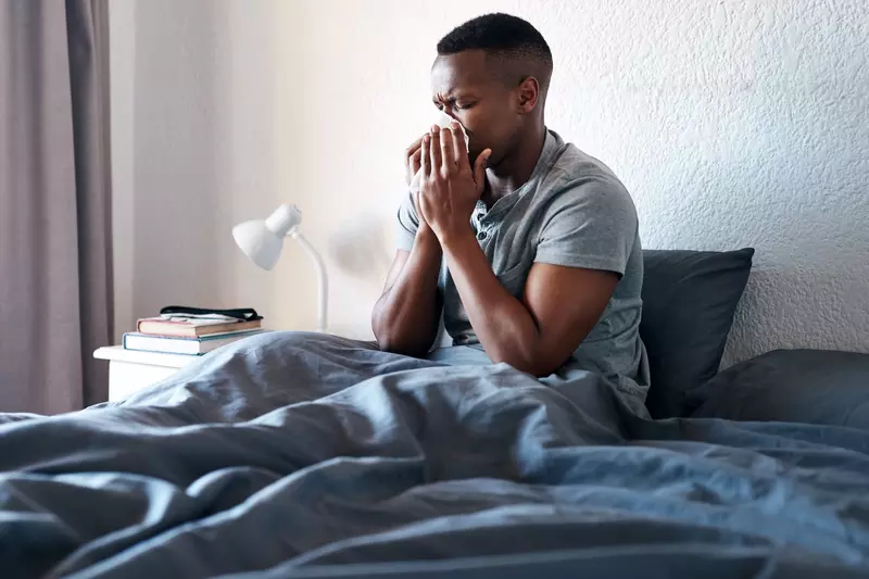 A man sneezing in bed. 
