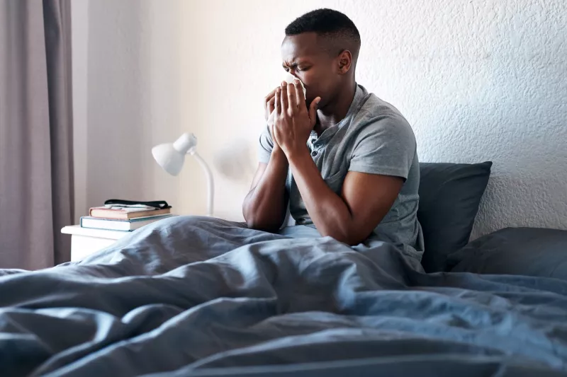 A man sneezing in bed.