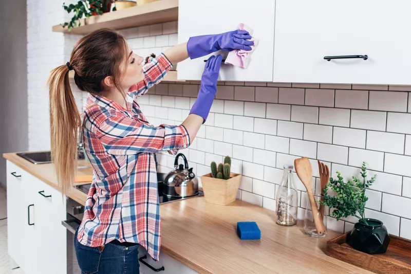 A young woman cleans the cabinets in her kitchen
