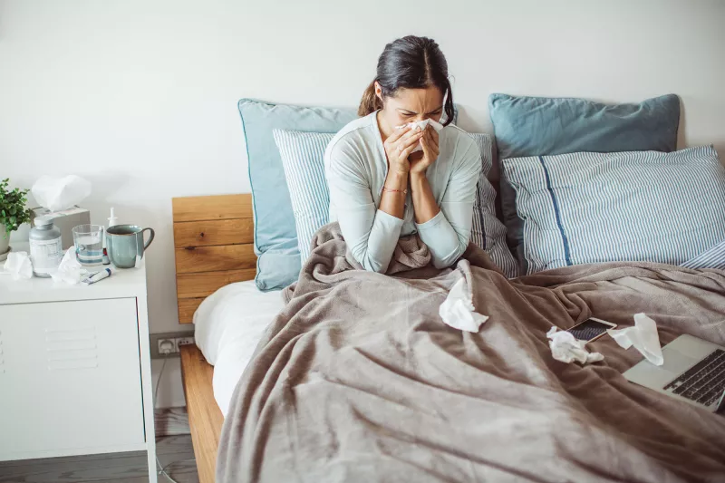 A woman sneezes as she sits sick in her bed