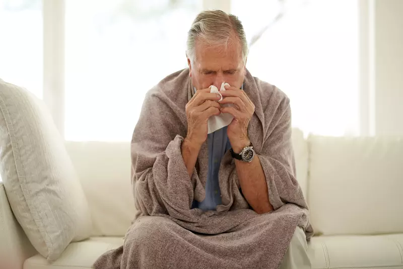 A man sneezing while at home on his couch. 