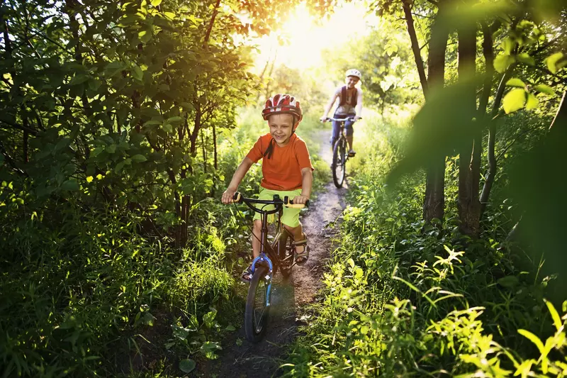 A boy races his bike ahead of his mom on the trail