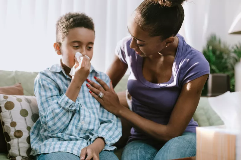 A mom comforts her son while he's sneezing at home.