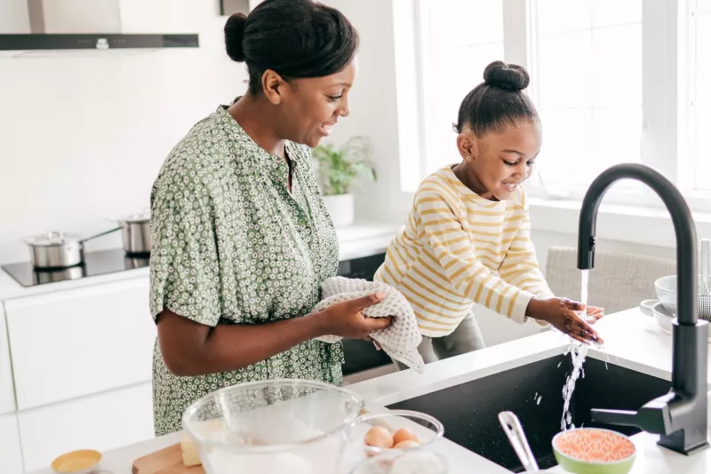 A mother and daughter wash their hands in the kitchen.