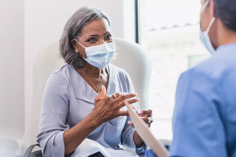 A mature woman visiting her doctor while wearing a mask.