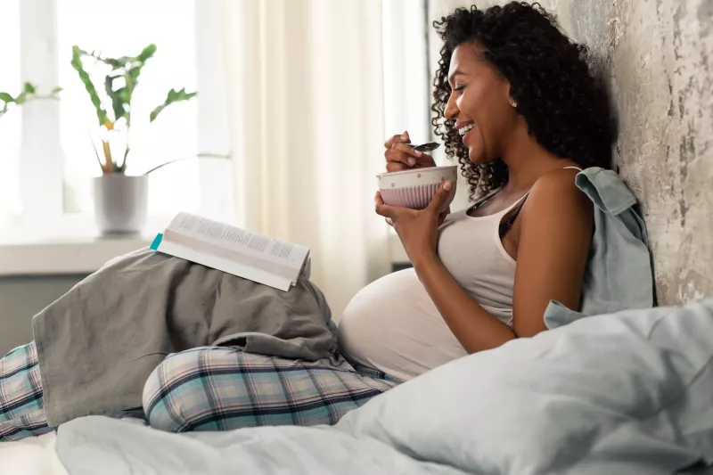 A pregnant woman eating breakfast in bed.