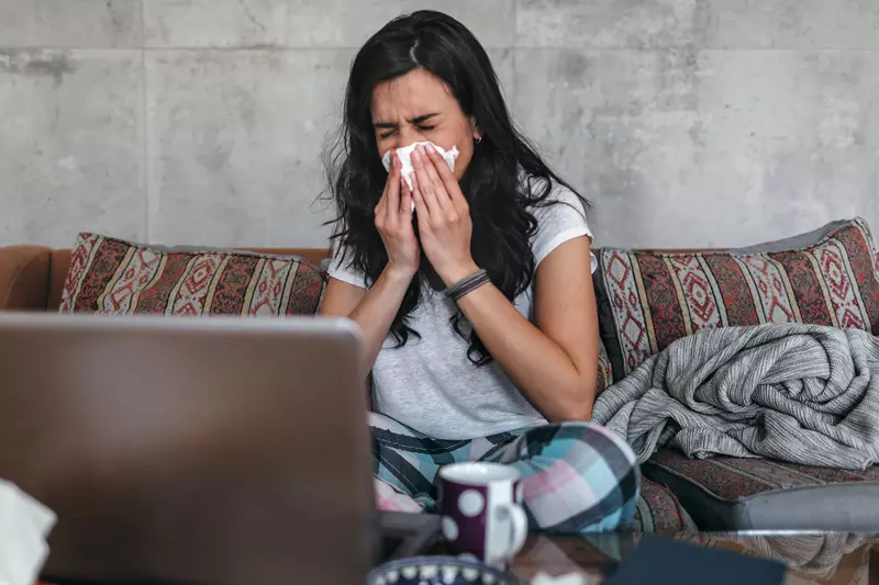 A woman sneezes into a tissue at home