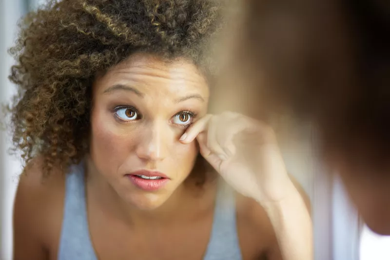 A woman examines her eye in a mirror.
