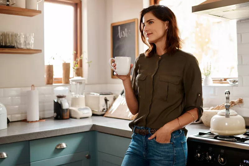 A woman drinking tea in her kitchen.