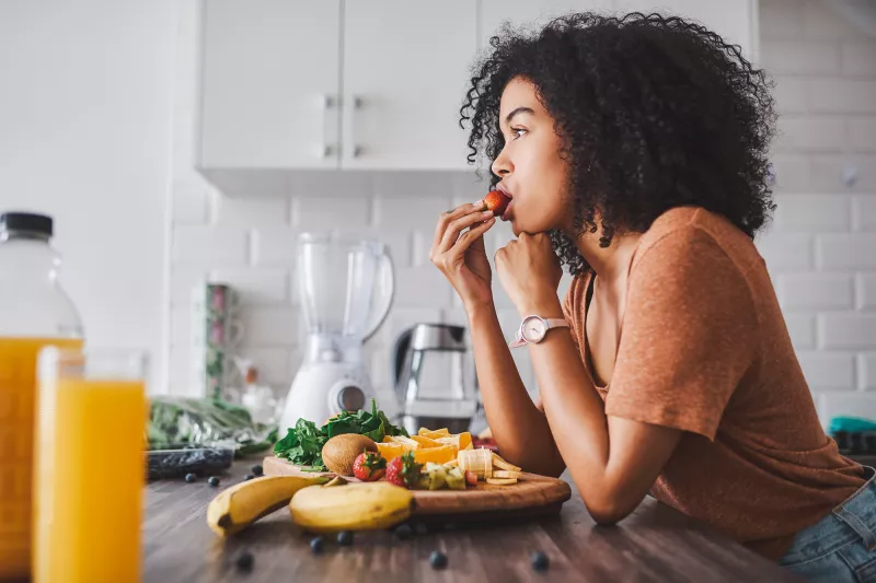 A woman eating a plate of fruit in her kitchen