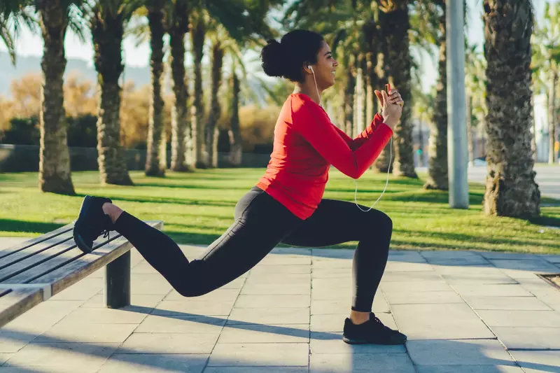 A woman doing a lunge outdoors on a bench.