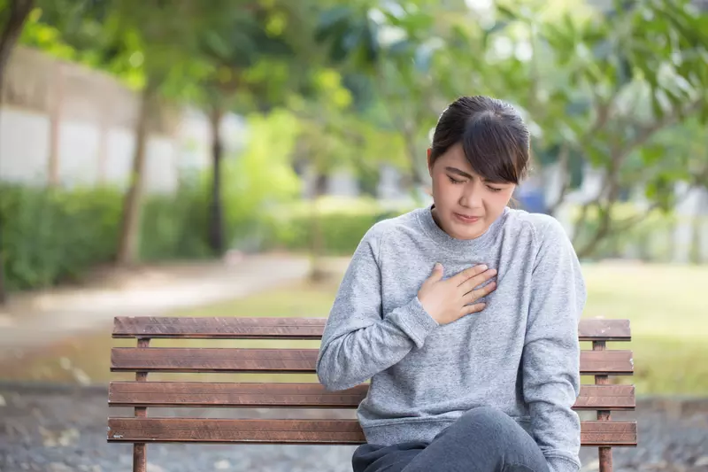Adult woman experiencing heartburn on a bench outside