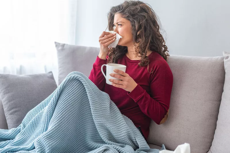 A woman on her couch blowing her nose.