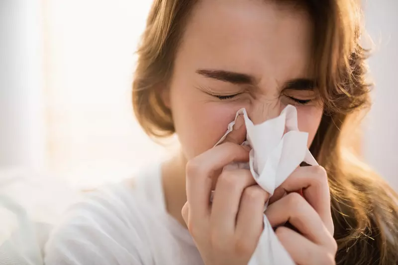 A sick woman blowing her nose into a tissue.