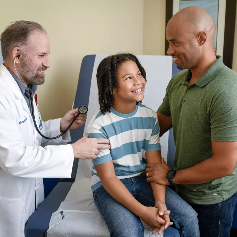 A Provider Checks a Child Patient's Breathing While His Father Supports Him