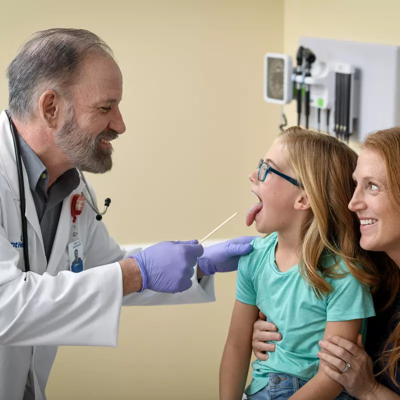 A Doctor Uses a Tongue Depressor to Check a Child Patient While Mom Holds Her