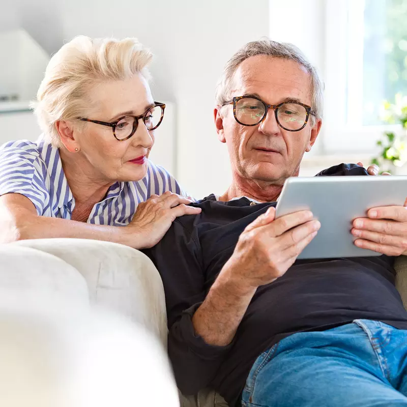 A Senior Couple Looks at a Tablet Together in Their Living Room.