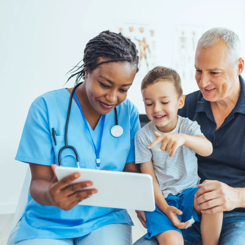 A Doctor Reviews a Patient's Chart with a Pediatric Patient and His Father in an Exam Room.