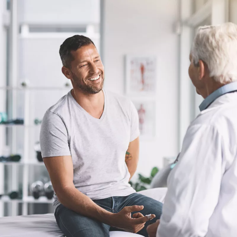 A Man Smiles as He Speaks to His Provider in an Exam Room