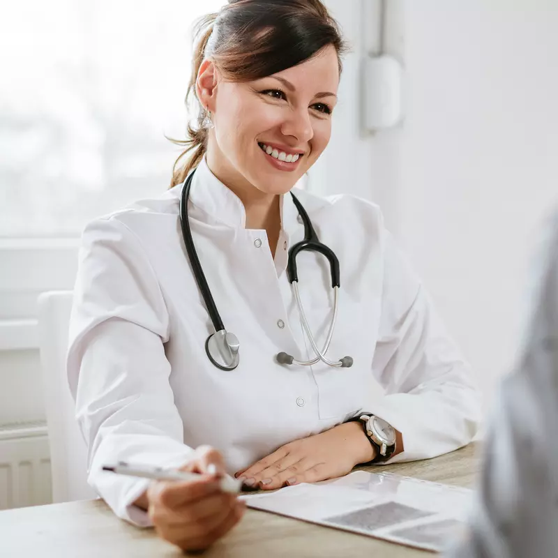 A friendly doctor meets a patient for the first time. They are both sitting at a desk, facing each other.