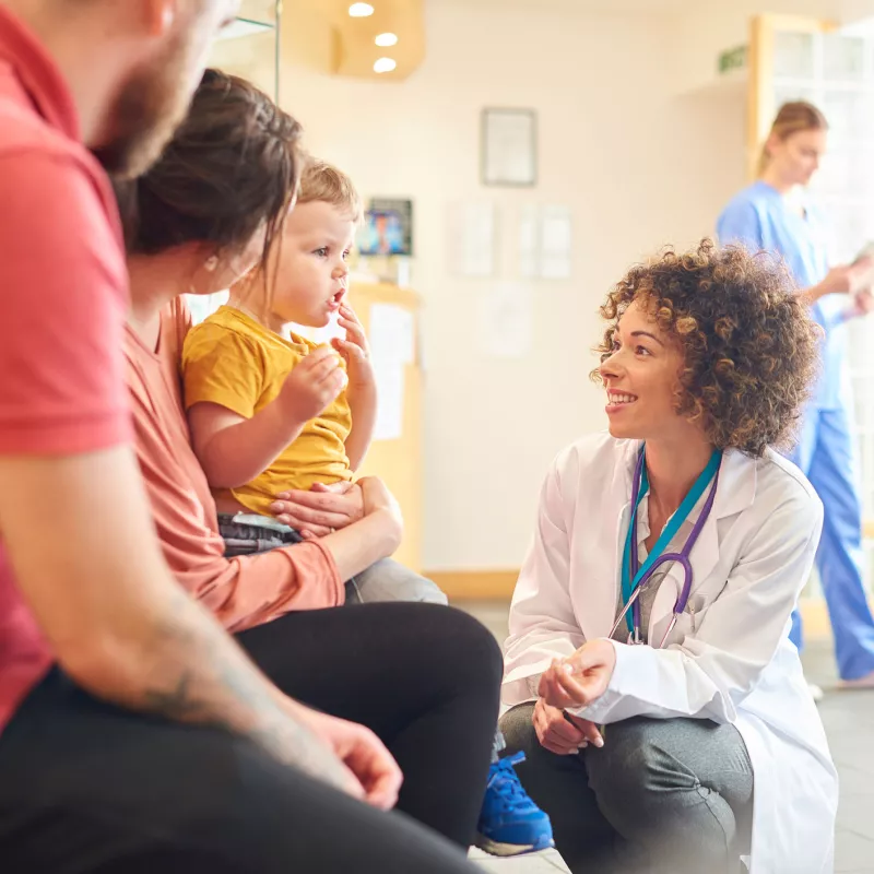 A doctor kneeling down and talking to a family's infant boy