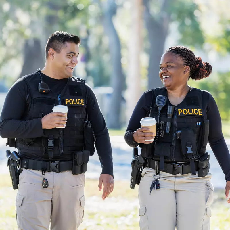 Two Police Enjoy a Cup of Coffee as They Walk Through a Park