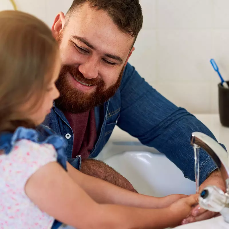 A dad teaches his young daughter how to wash her hands