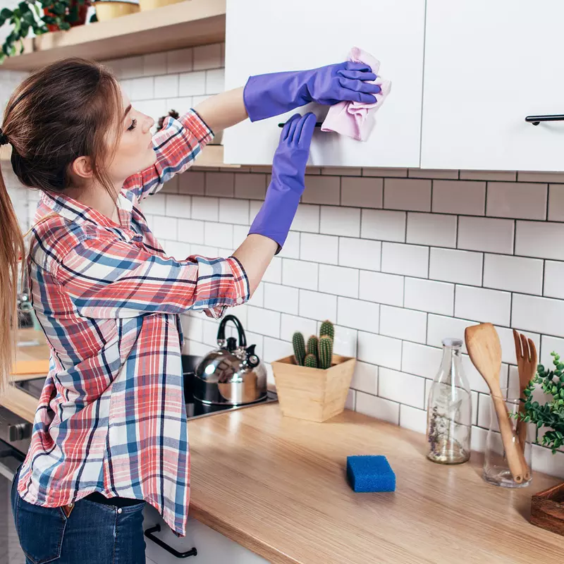 A young woman cleans the cabinets in her kitchen