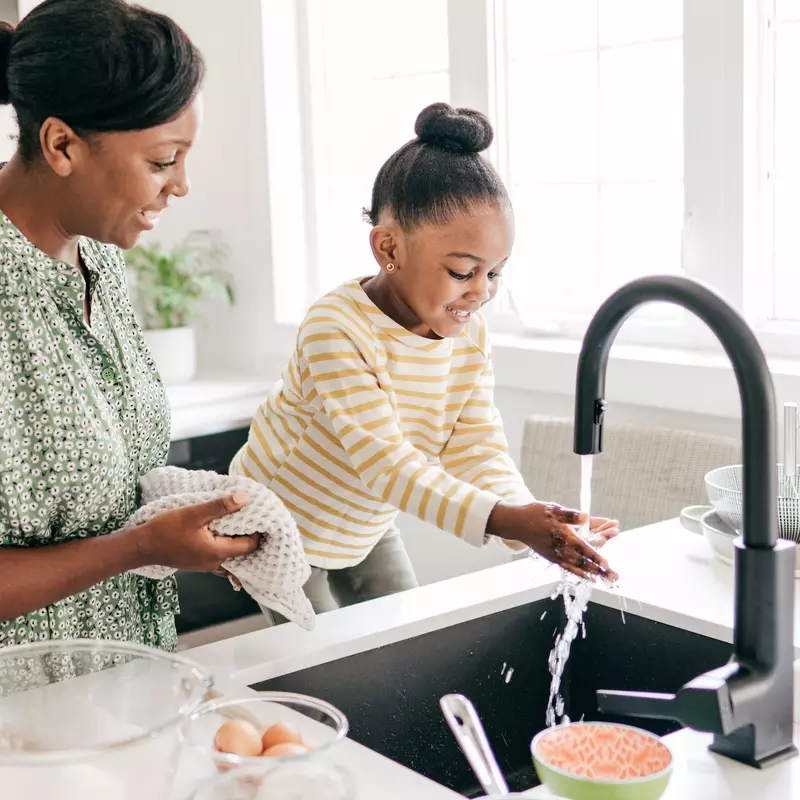 A mother and daughter wash their hands in the kitchen. 