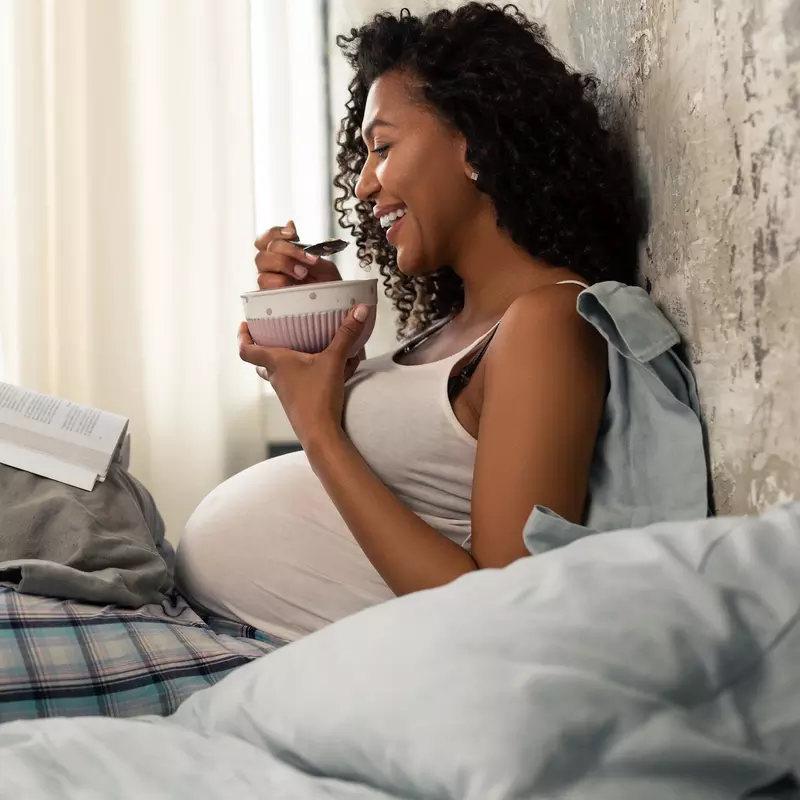 A pregnant woman eating breakfast in bed.