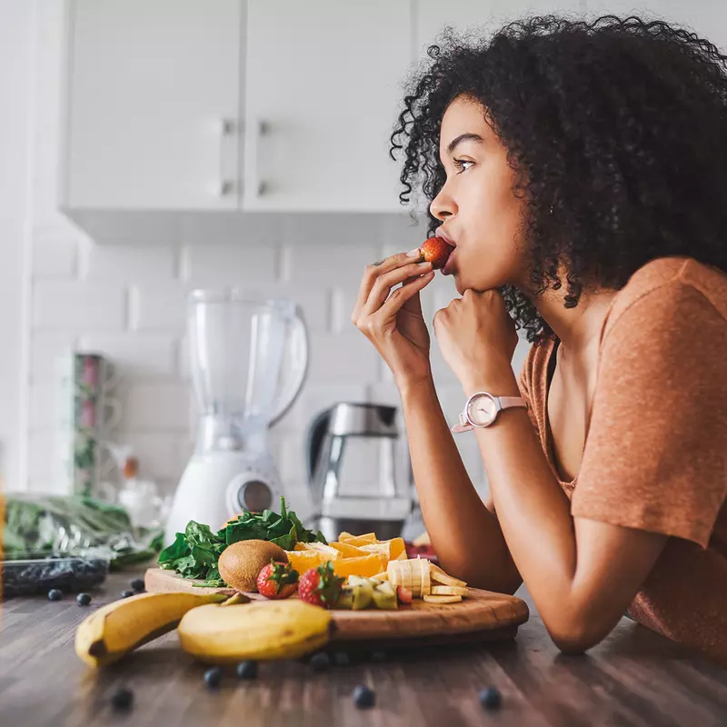 A woman eating a plate of fruit in her kitchen