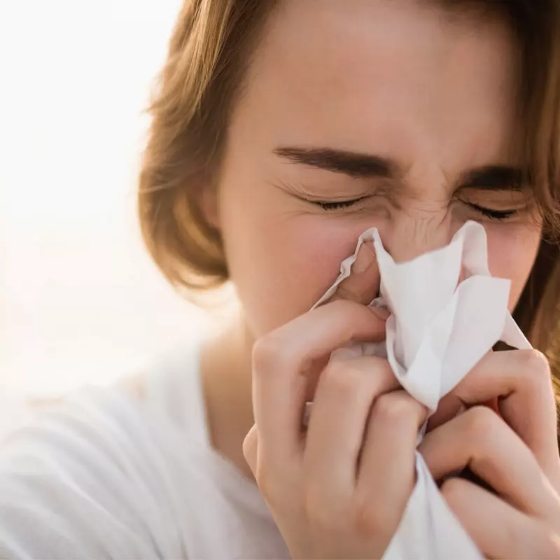 A sick woman blowing her nose into a tissue.