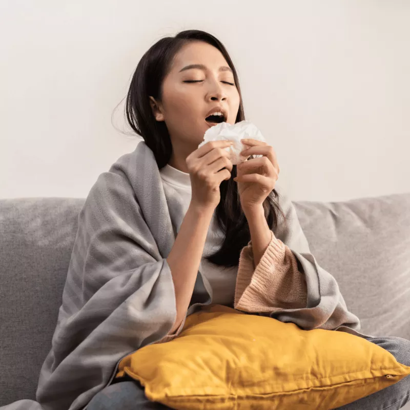 A woman sneezing into a tissue.