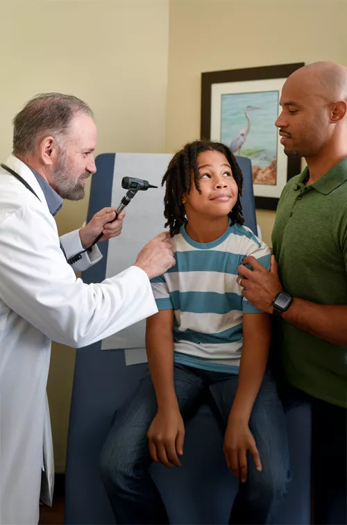 A Centra Care Provider Checks a Child Patient's Ears While His Father Supports Him